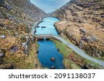 Aerial view of the stone Wishing Bridge over winding stream in green valley at Gap of Dunloe in Black Valley of Ring of Kerry, County Kerry, Ireland