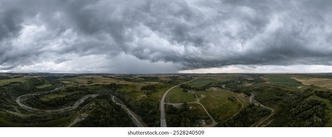 Aerial view of storm clouds sweeping over the vast green landscape of Alberta, Canada, showcasing rolling hills, winding roads, and a sense of impending weather change. - Powered by Shutterstock