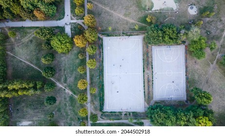 Aerial View Of Street Basketball Court. Kids Are Playing Football In The Field. Aerial Outdoor Basketball Court With Players Overhead Shot Top Down View, Daytime.