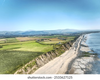 Aerial view of a stunning coastal landscape with green fields, cliffs, and a sandy beach under a clear blue sky. - Powered by Shutterstock