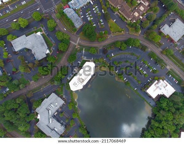 Aerial view. Suburb. Asphalt\
parking for cars and roads. Green bushes, trees. Roofs of one-story\
houses. Environmental and social issues, construction, housing\
issue.