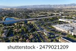 Aerial view of a suburban area with a highway, residential buildings, and a small lake in San Jose, California with mountains in the background.