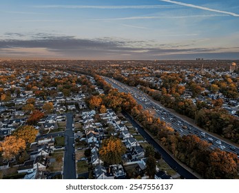 Aerial view of suburban neighborhood with autumn foliage and highway traffic at sunset, capturing the vibrant colors of fall in the cityscape. - Powered by Shutterstock