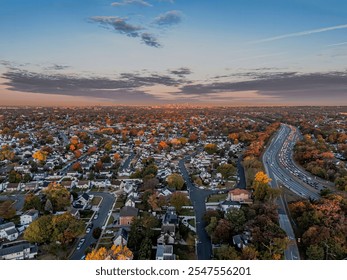 Aerial view of suburban neighborhood with autumn foliage and highway traffic at sunset, capturing the skyline in the distance. - Powered by Shutterstock