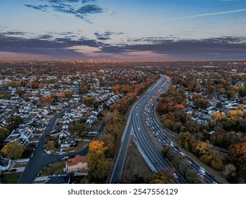 Aerial view of a suburban neighborhood with a busy highway at sunset, showcasing autumn foliage and distant city skyline. - Powered by Shutterstock