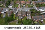 Aerial view of a suburban neighborhood with rows of houses, green lawns, and parked cars on a sunny day.