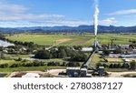 Aerial view of a sugar mill processing plant with smoke stacks and distant mountains.