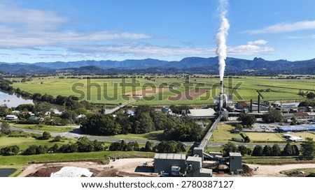 Aerial view of a sugar mill processing plant with smoke stacks and distant mountains.