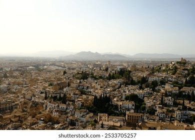 Aerial view of a sunlit Mediterranean city with tightly packed historic buildings, whitewashed facades, and lush greenery, set against rolling hills. - Powered by Shutterstock