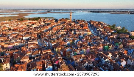 Aerial view at sunset, Burano Island with vibrant houses, canals, fishing boats, Church of Saint Martin Bishop, and Campanile, Venice, Italy