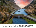 Aerial view of sunset at the stone Wishing Bridge over winding stream in green valley at Gap of Dunloe in Black Valley of Ring of Kerry, County Kerry, Ireland