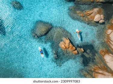 Aerial view of sup boards, blue sea, rocks at sunset in summer. People on floating canoe in transparent azure water. Kayak. Sardinia island, Italy. Tropical seascape. Active travel. Top drone view - Powered by Shutterstock