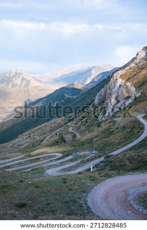 Aerial view of SUVs navigating a sharp switchback dirt road on a steep green mountain slope during the day