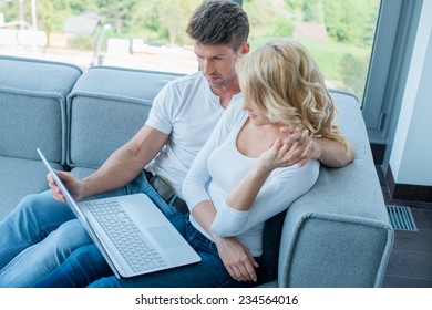 Aerial View of Sweet White Couple Sitting on Gray Sofa at the Living Room While Watching Something on Laptop Computer.
