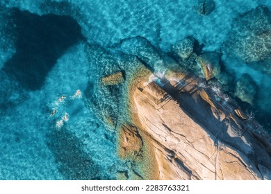 Aerial view of swimming people in blue sea, rocky beach, waves at sunset in summer in Sardinia, Italy. Tropical background. Landscape. Transparent azure water and stones. Top drone view. Down view