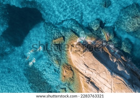 Aerial view of swimming people in blue sea, rocky beach, waves at sunset in summer in Sardinia, Italy. Tropical background. Landscape. Transparent azure water and stones. Top drone view. Down view