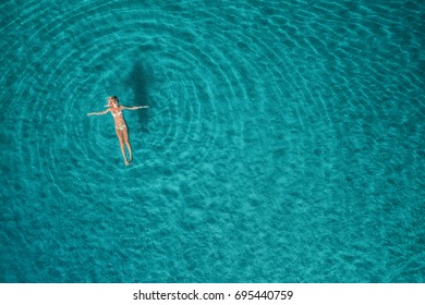 Aerial view of swimming woman in Blue Lagoon. Mediterranean sea in Oludeniz, Turkey. Summer seascape with girl, clear azure water, waves at sunrise. Transparent water.Top view from flying drone.Travel