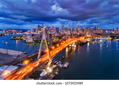 Aerial view of Sydney city CBD landmarks on Sydney harbour behind steel cables and archs of Anzac bridge highway connecting Inner West Victoria road with Western Distributor at sunset with lights. - Powered by Shutterstock