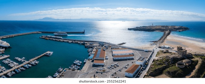 Aerial view of Tarifa, Spain, featuring a bustling harbor with boats, a ferry, sandy beaches, Isla de las Palomas with a lighthouse, and the Strait of Gibraltar. - Powered by Shutterstock