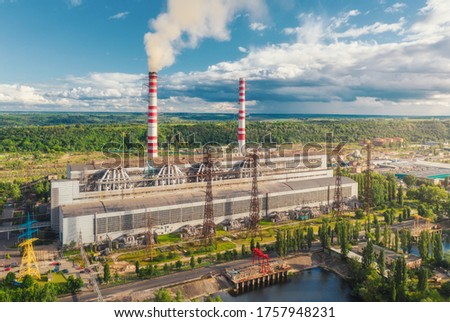 Aerial view of thermal power station. Industrial landscape with thermal power plant, pipes with smoke, buildings, green trees, blue sky with clouds at sunset in summer. Top view. Smoke stack