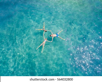 Aerial view of three young friends holding hands and make a star formation in the transparent turquoise sea. Top view of group of friends floating in the water. Thailand, Phuket, Andaman sea.