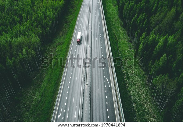 Aerial view of toll road highway with cars and\
trucks through green summer\
forest