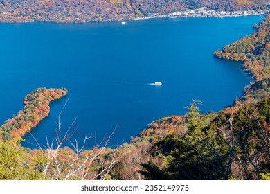 Aerial view of tour boats cruising on Lake Chuzenji 中禅寺湖 on a sunny autumn day, in Nikko National Park, Tochigi Prefecture, Japan, with beautiful fall colors on the lakeside hills and Hachodeshima