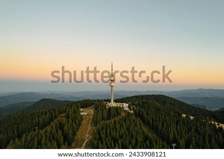 Aerial view tower structure high in mountains aerial view drone forward, dense pine forest at sunrise in summer morning on blue sky. Panorama post-dawn blue sky high in mountains. Nature Bulgaria