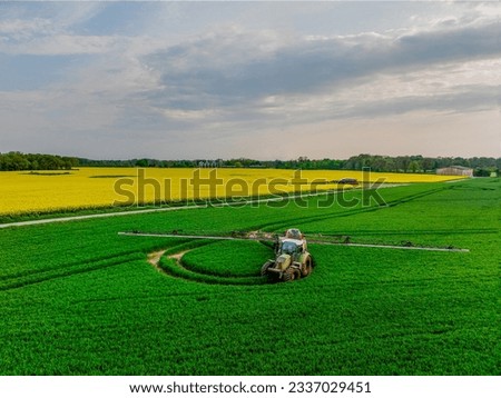 Aerial view of tractor with fertilizer spreader in wheat field. Aerial view of tractor with sprayer against diseases. Application of water-soluble fertilizers, pesticides or herbicides in the field. 