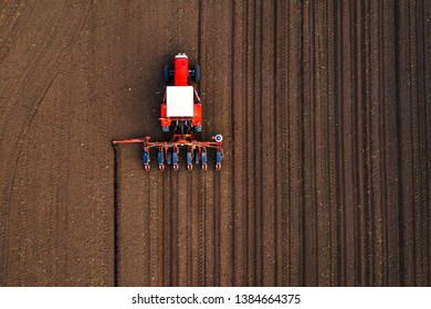 Aerial view of tractor with mounted seeder performing direct seeding of crops on plowed agricultural field. Farmer is using farming machinery for planting process, top view - Shutterstock ID 1384664375