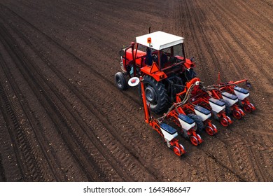 Aerial View Of Tractor With Mounted Seeder Performing Direct Seeding Of Crops On Plowed Agricultural Field. Farmer Is Using Farming Machinery For Planting Process.