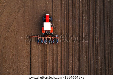Aerial view of tractor with mounted seeder performing direct seeding of crops on plowed agricultural field. Farmer is using farming machinery for planting process, top view