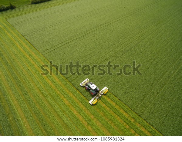 Aerial view of a tractor mowing a green fresh grass\
field, \
a farmer in a modern tractor mowing a green fresh grass\
field on a sunny day