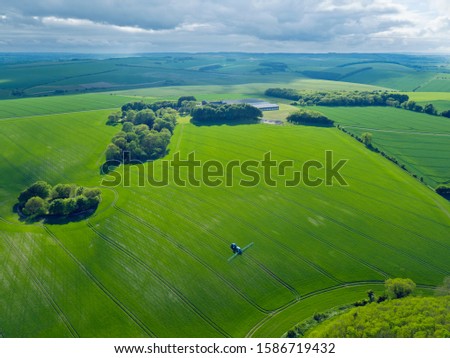 Aerial view of tractor spraying crop in green farm fields with pesticide
