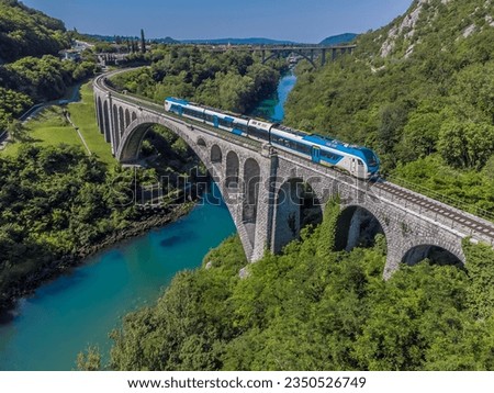 An aerial view of a train crossing the stone railway bridge on the outskirts of the town of Solkan in Slovenia in summertime