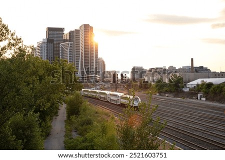 Aerial view of a train passing by district with highrise tall buildings in city center at sunset sunrise hour, Toronto Canada. Commute and, public transit infrastructure, green transportation concept.