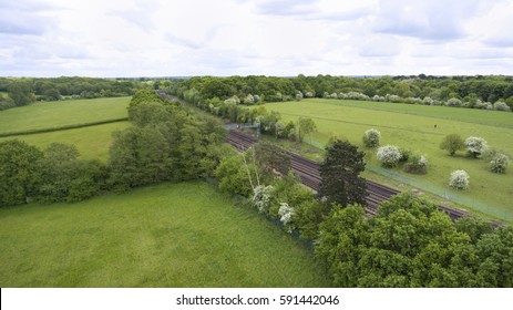 Aerial View Of Train Rail Tracks Crossing Green Fields And Forests In South East England , On A Summer Day .