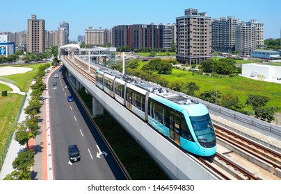 Aerial View Of A Train Traveling On The Elevated Track Of Danhai Light Rail System Near Tamsui District Office Station With Residential Towers Standing Under Sunny Sky In Background In New Taipei City