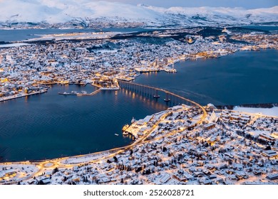 Aerial view of Tromso, Norway with city lights in winter from Storsteinen mountain. Tromsoya island with snowy roofs of Tromso town, harbor, Sandnessundet bridge over Fjord and mountains in background - Powered by Shutterstock