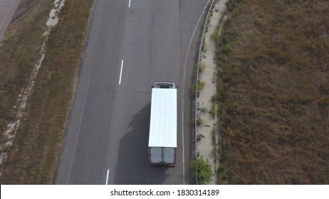 Aerial view of truck with white cargo trailer driving on road to destination. Flying over lorry moving through countryside highway. Concept of logistic or delivery. Top view Slow motion.