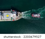 Aerial view of tug boat assisting big bulk carrier cargo ship. Large ship escorted by tugboat.