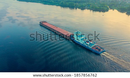 
Aerial view of a tugboat sailing down the river and pushing a barge in front of it. Volga river. Photo taken from a drone.