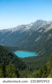 Aerial view of turquoise alpine mountain lake Lago di Anterselva (Antholzer See) as seen from Passo Stalle (Staller Pass) in a Dolomite mountain valley with green pine forest