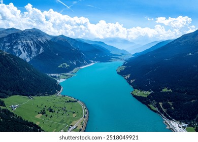 Aerial view of the turquoise lake surrounded by mountains and lush greenery in a picturesque valley on a sunny day - Powered by Shutterstock