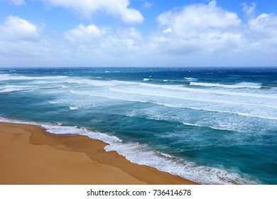 Aerial view turquoise waves push ashore on yellow sand beach, land meets sea. Great Ocean Road, Australia.