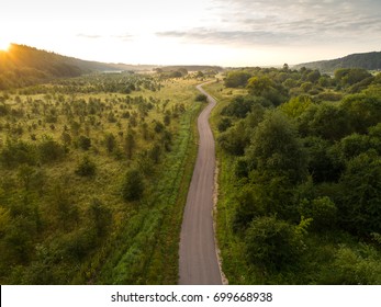 Aerial view of twisting road among the forest and trees. Sunset field in Lithuania.