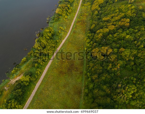 Aerial view of twisting road among the river\
and forest. Sunset field in\
Lithuania.