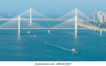 Aerial view of two iconic cable-stayed bridges spanning turquoise waters with cargo ships and cityscape in background