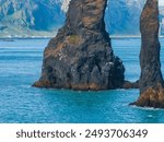 Aerial view of two large black rock formations creating a natural archway in the ocean with a hazy blue mountain range in the background, Iceland.