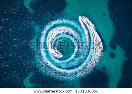 Aerial view of two motorboats forming a circle of waves and bubbles with their engines over turquoise sea